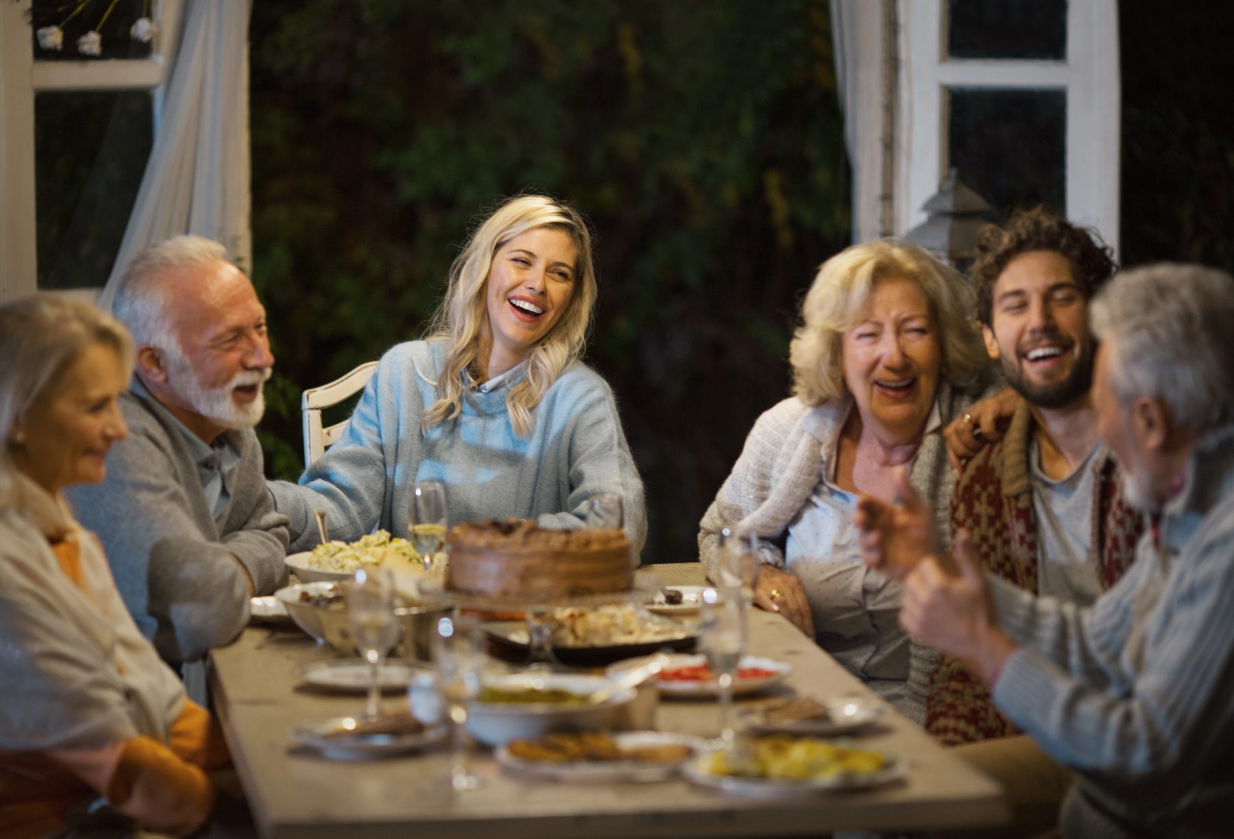 Three generations of a family talking and laughing together over tea at the kitchen table.